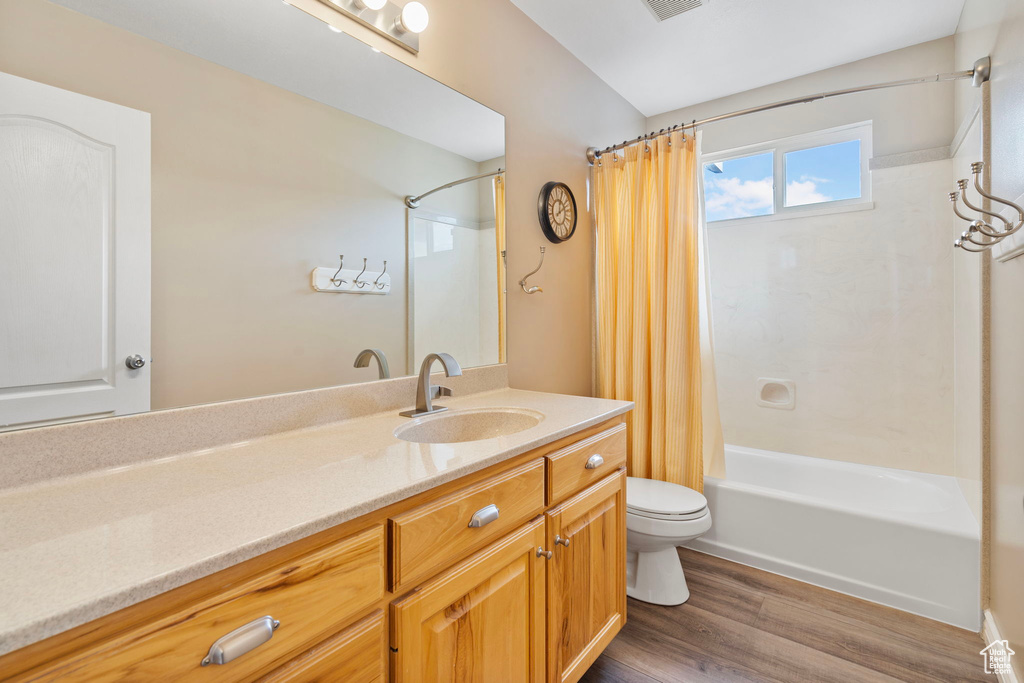 Full bathroom with oversized vanity, toilet, shower / tub combo, and wood-type flooring