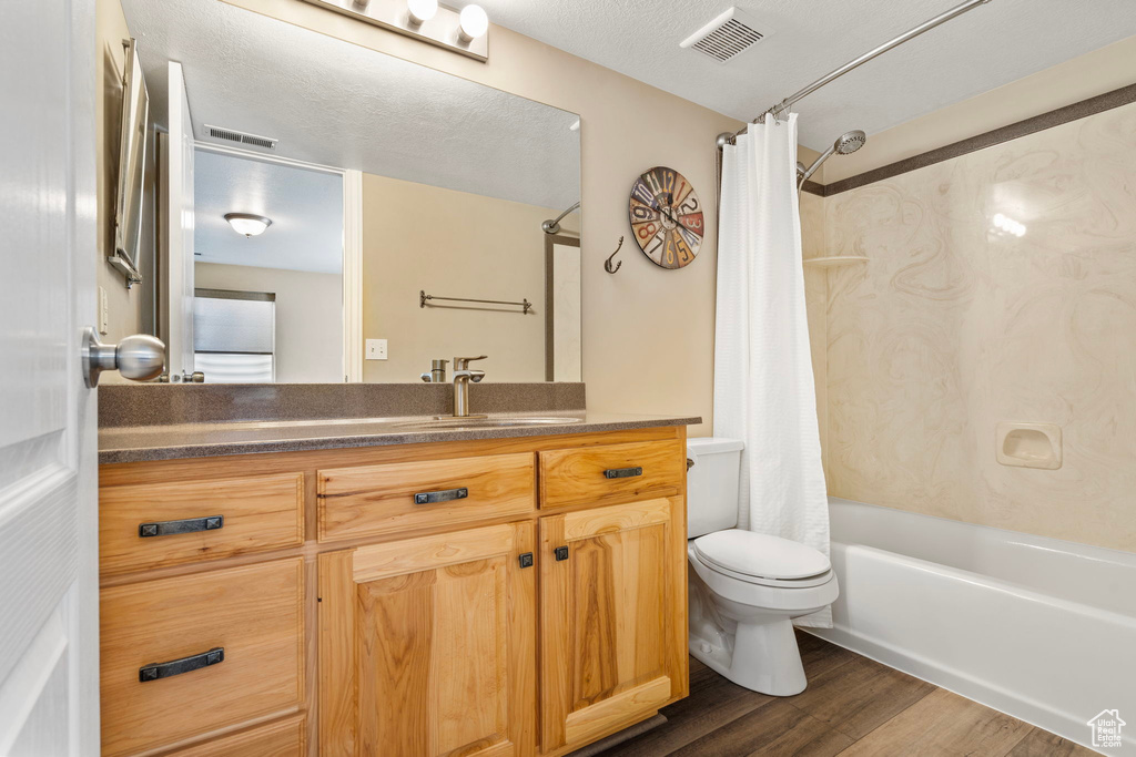 Full bathroom featuring vanity, shower / bath combo, wood-type flooring, a textured ceiling, and toilet