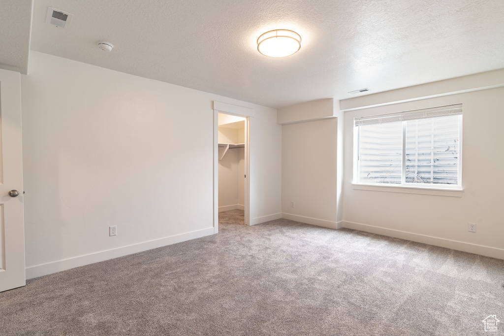 Unfurnished bedroom featuring a closet, light carpet, a spacious closet, and a textured ceiling