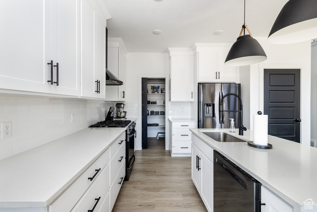 Kitchen featuring light hardwood / wood-style floors, backsplash, white cabinets, black gas stove, and stainless steel fridge
