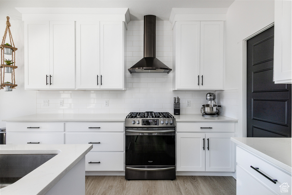 Kitchen with tasteful backsplash, black range with gas stovetop, wall chimney exhaust hood, and light hardwood / wood-style floors