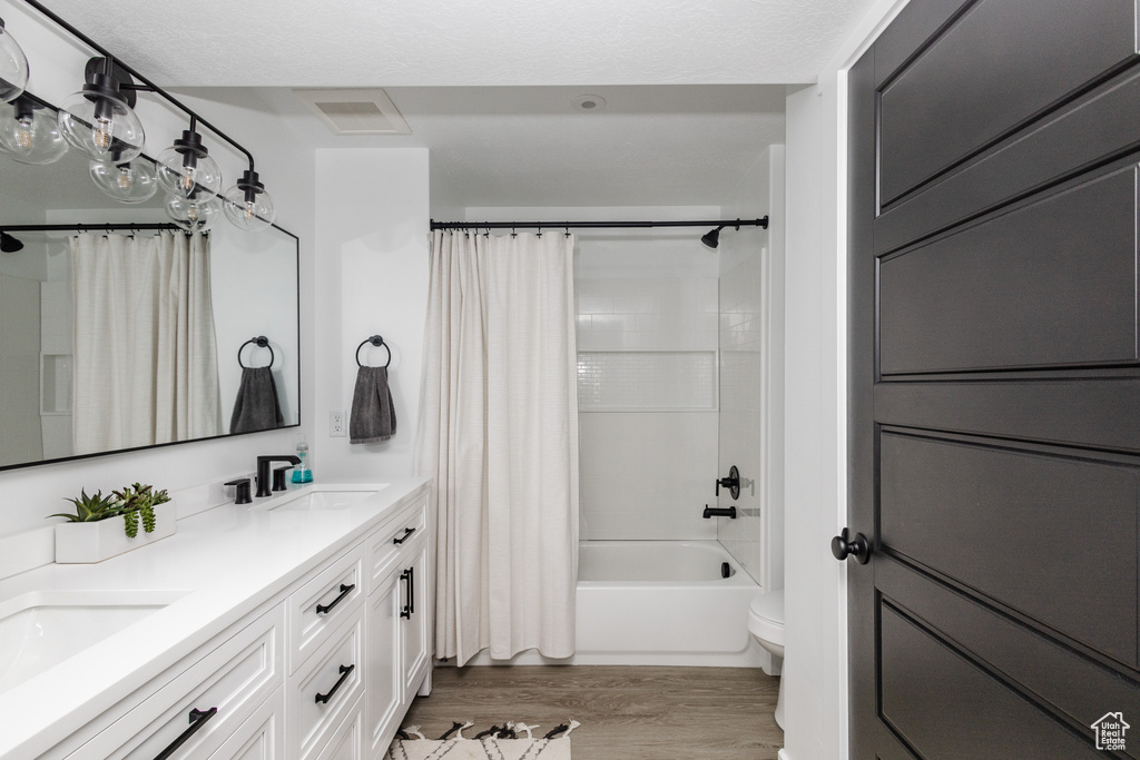 Full bathroom featuring toilet, double sink vanity, shower / tub combo with curtain, and hardwood / wood-style flooring