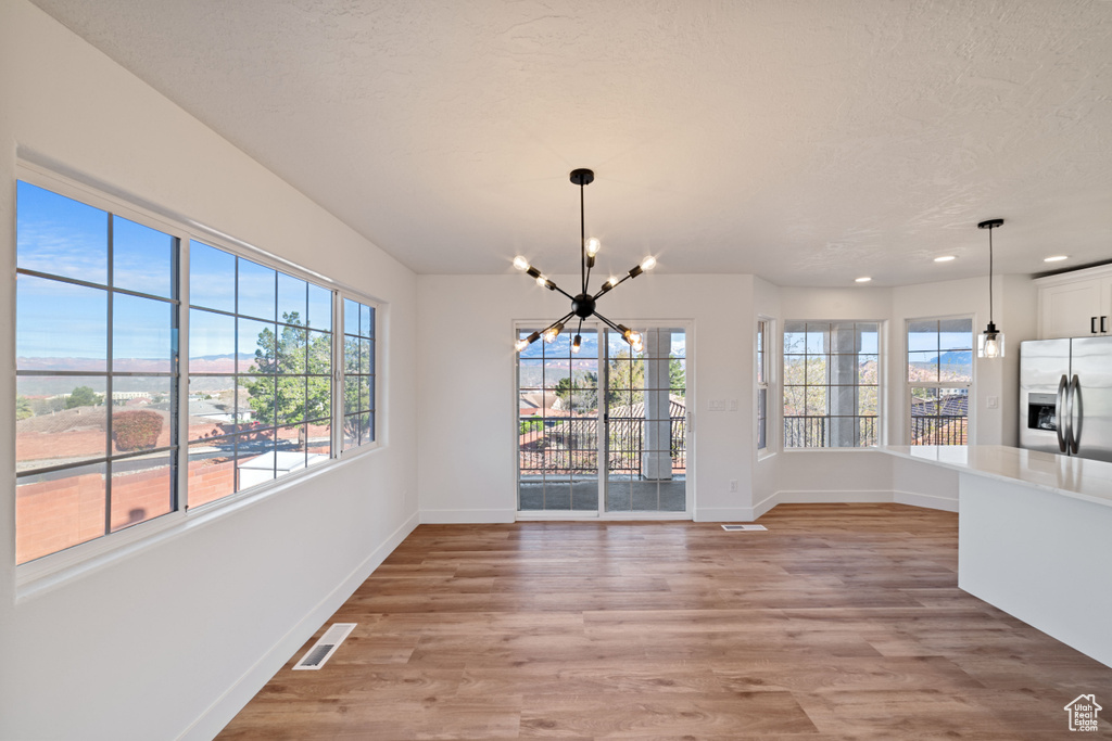 Unfurnished dining area with plenty of natural light, light hardwood / wood-style floors, and a notable chandelier