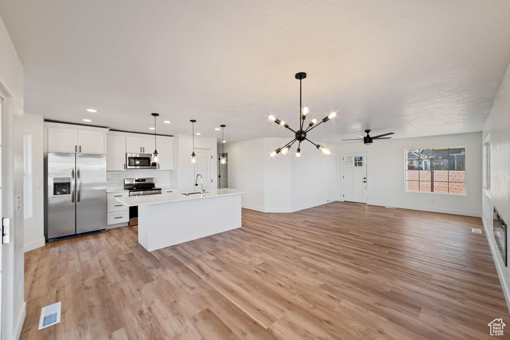Kitchen featuring light hardwood / wood-style floors, white cabinets, stainless steel appliances, decorative light fixtures, and sink