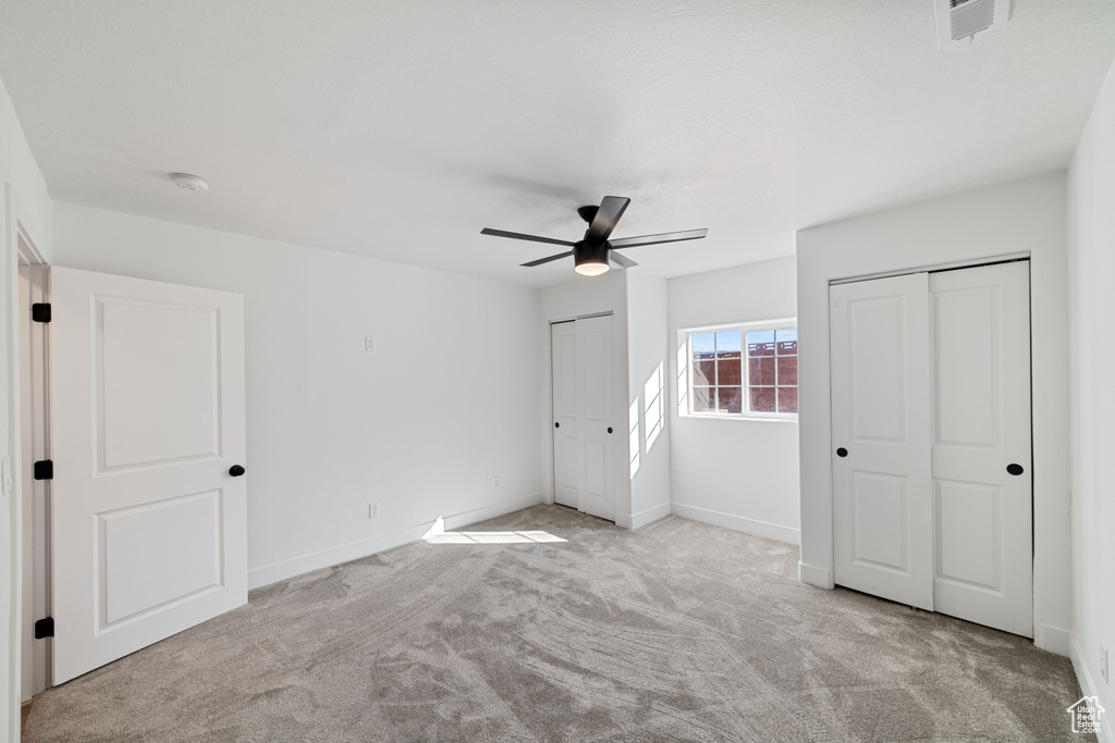 Unfurnished bedroom featuring light colored carpet, two closets, and ceiling fan
