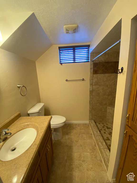Bathroom with vanity, tile floors, toilet, lofted ceiling, and a textured ceiling