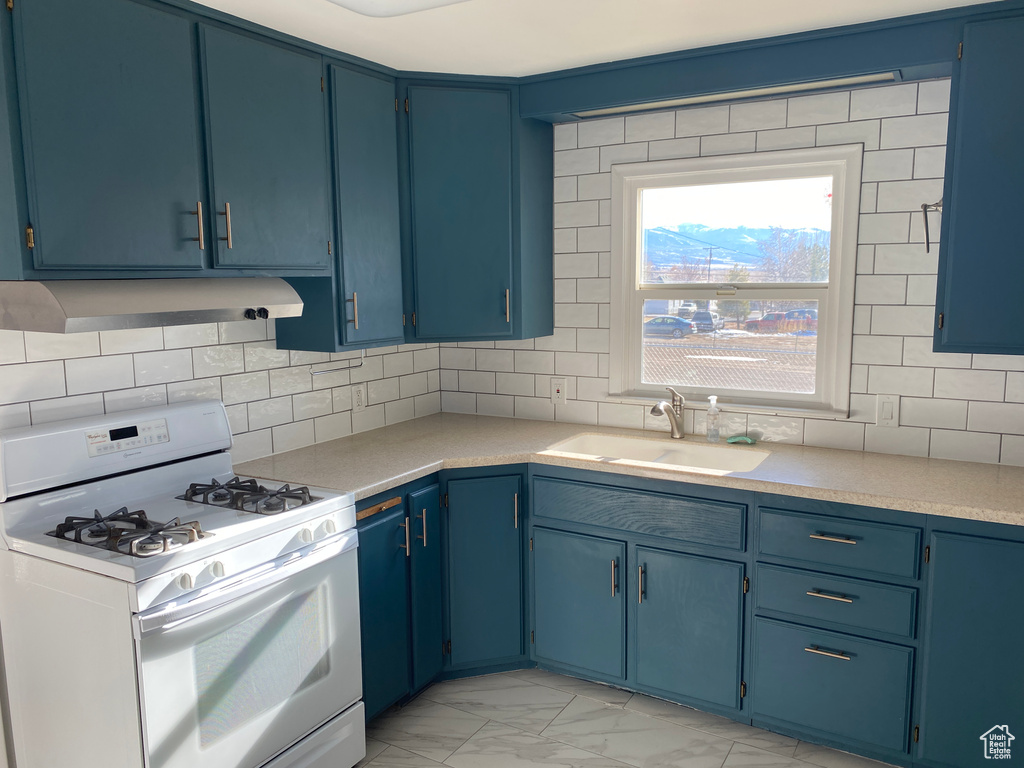 Kitchen featuring white range with gas stovetop, sink, blue cabinets, and light tile floors