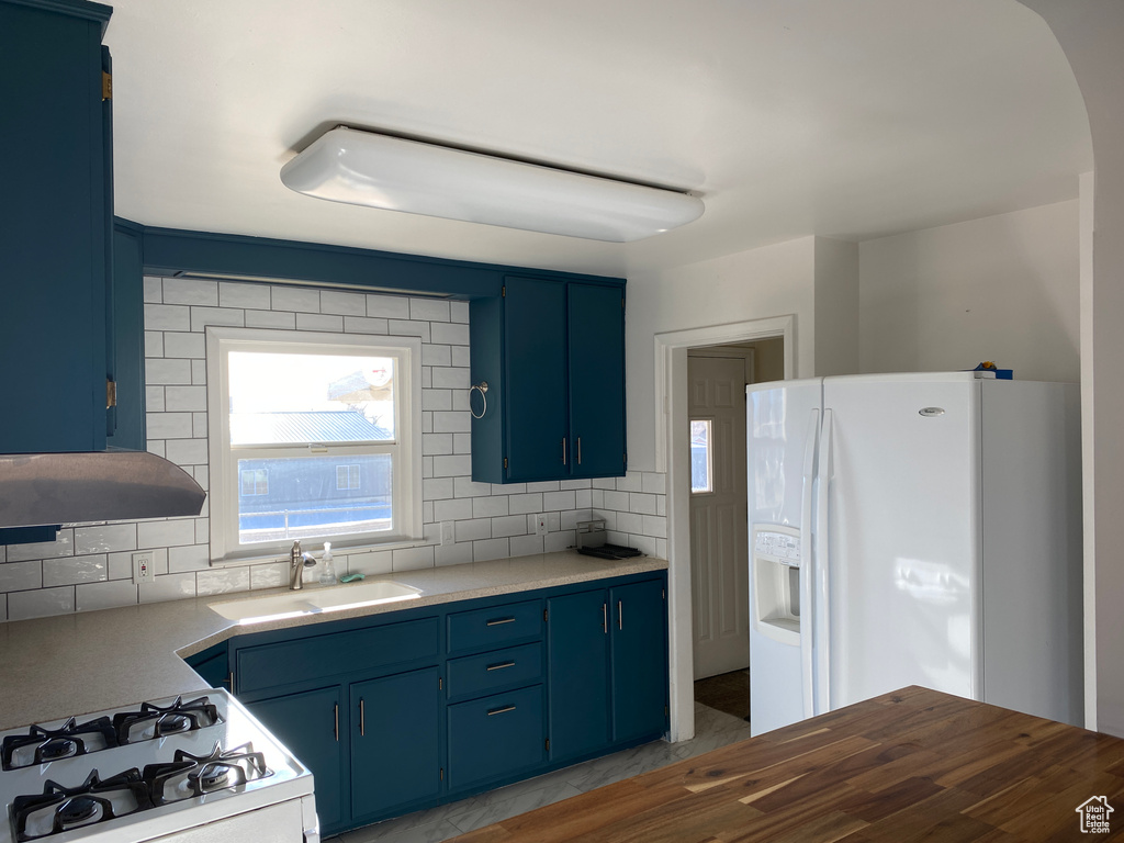 Kitchen featuring blue cabinets, white refrigerator with ice dispenser, range, and tasteful backsplash