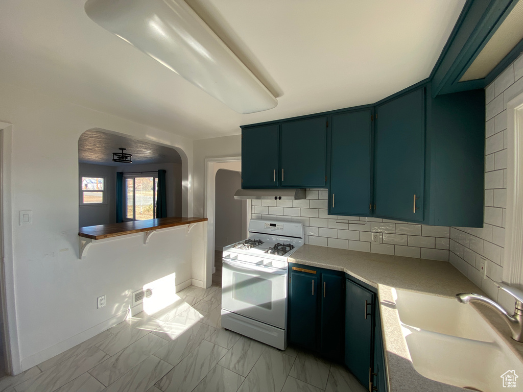 Kitchen featuring white gas range oven, backsplash, sink, and light tile floors