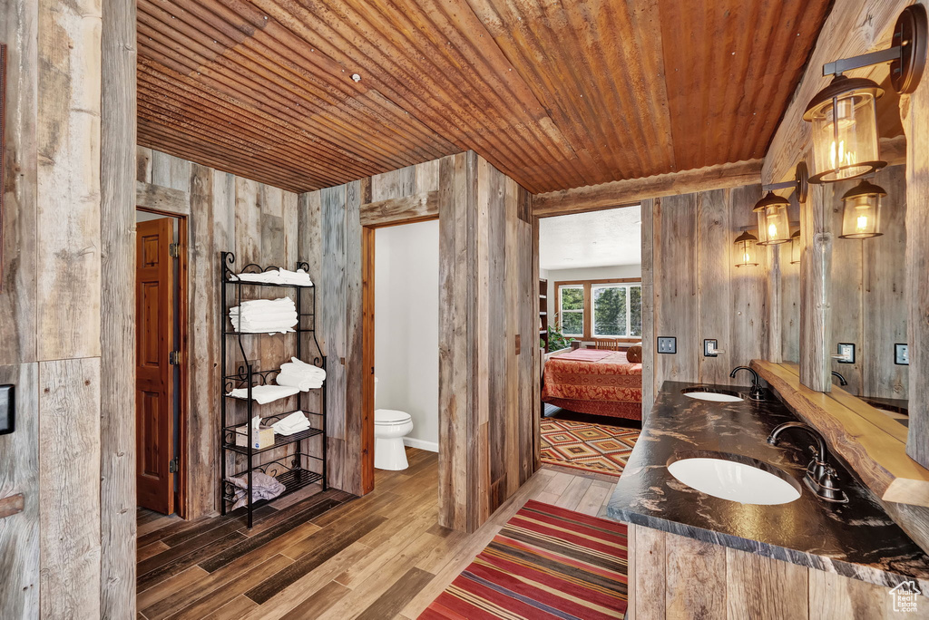 Bathroom featuring wood-type flooring, double vanity, toilet, wood walls, and wooden ceiling