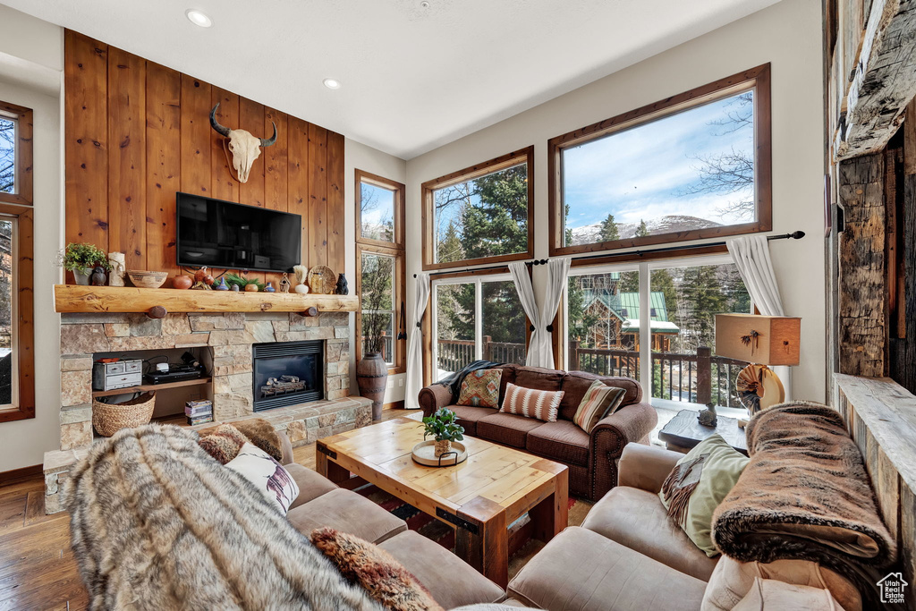 Living room with wood walls, hardwood / wood-style flooring, a healthy amount of sunlight, and a stone fireplace