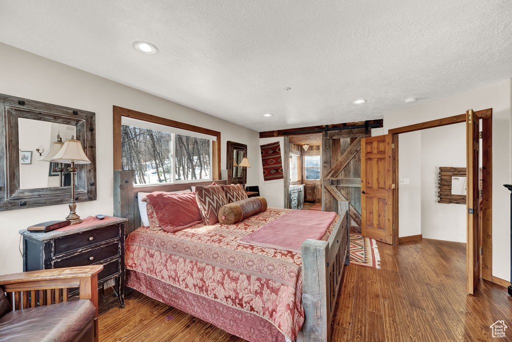 Bedroom featuring a barn door, a textured ceiling, and dark hardwood / wood-style floors