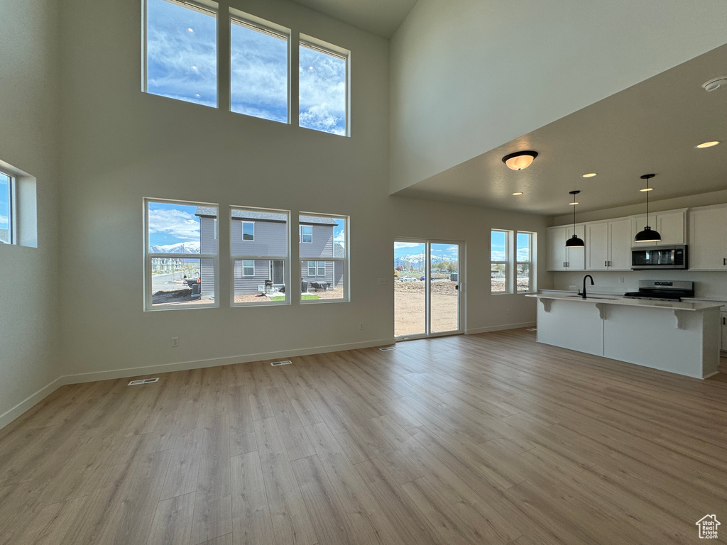 Unfurnished living room with sink, light hardwood / wood-style flooring, and a towering ceiling