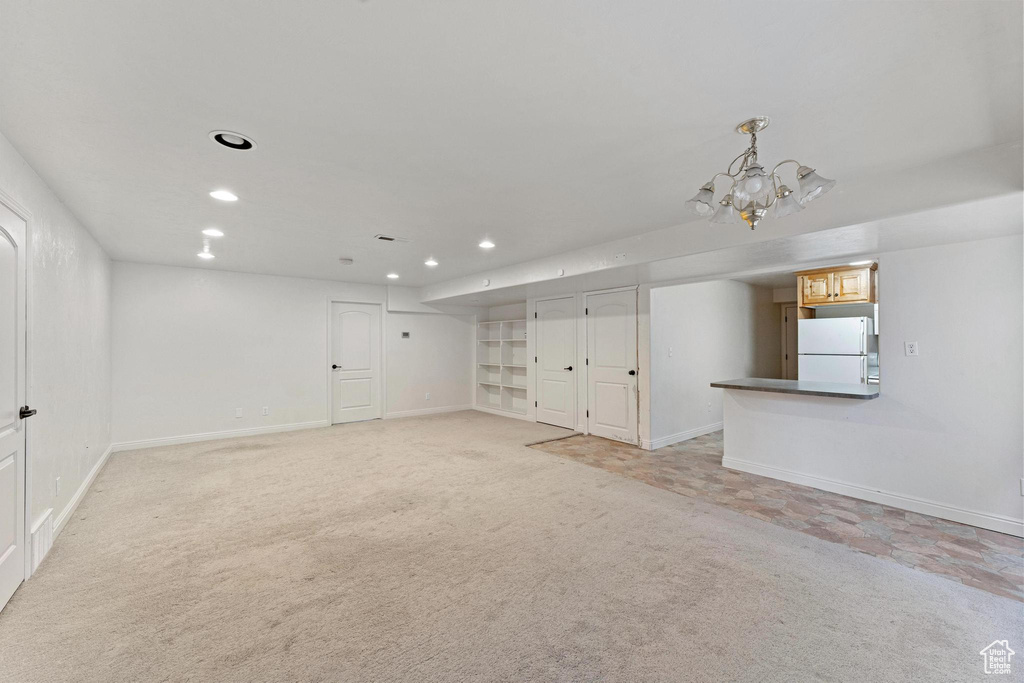 Basement with white fridge, an inviting chandelier, and light colored carpet