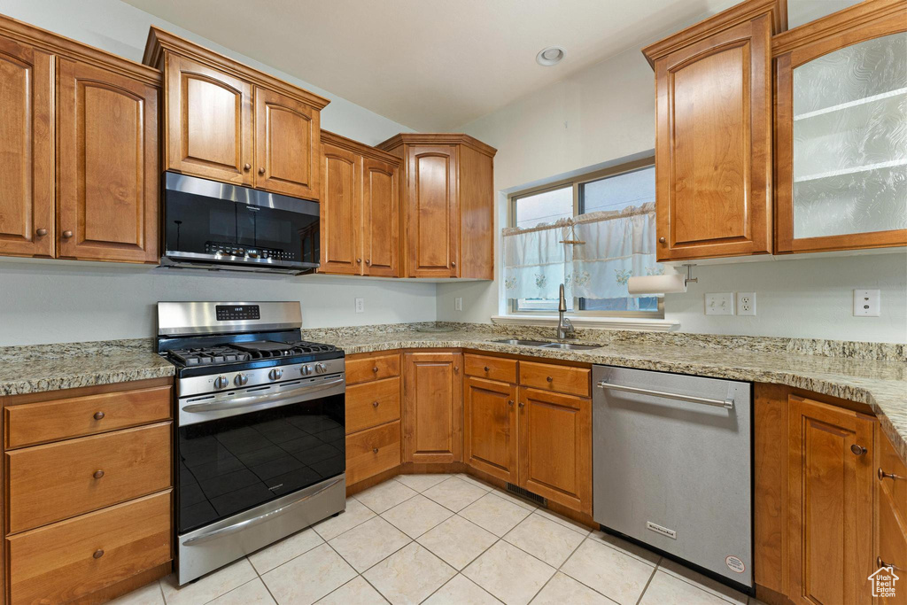 Kitchen with light stone counters, appliances with stainless steel finishes, sink, and light tile floors