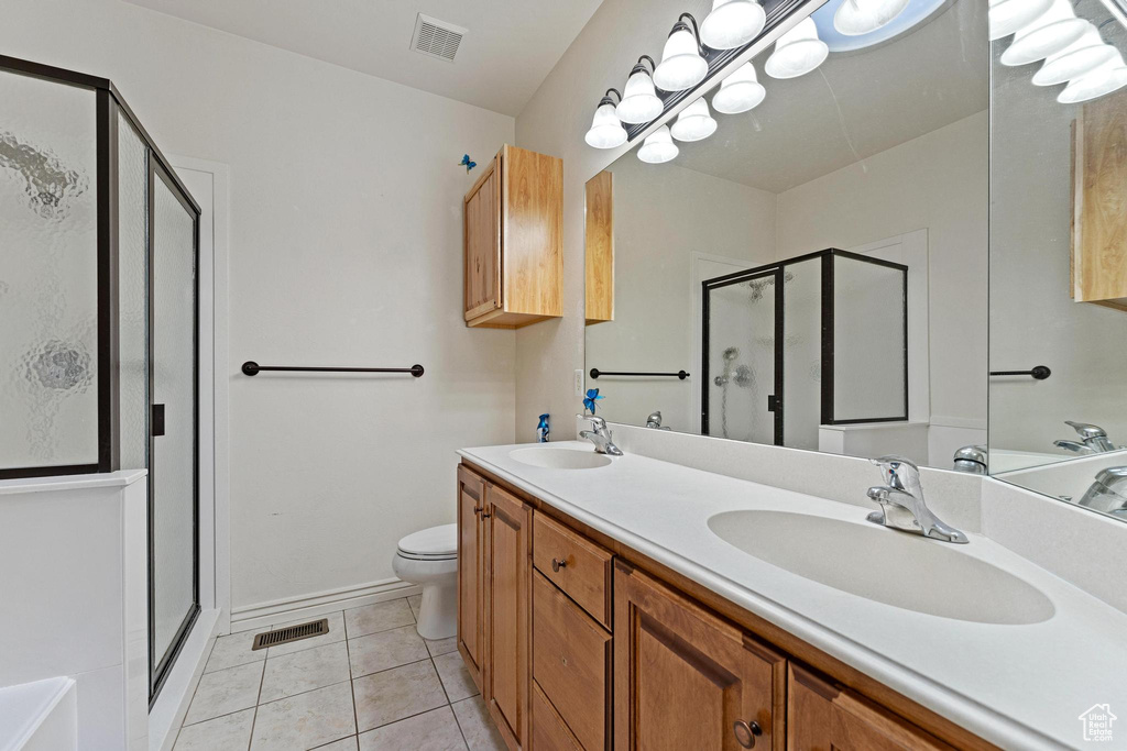 Bathroom with tile floors, dual vanity, toilet, and a shower with shower door