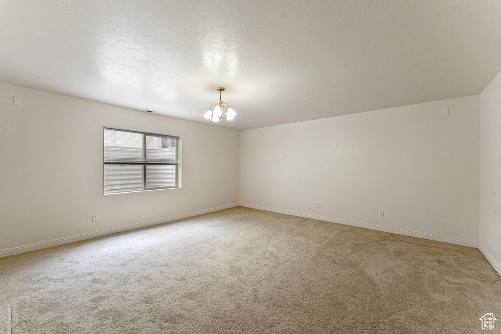Unfurnished room featuring light colored carpet and a notable chandelier