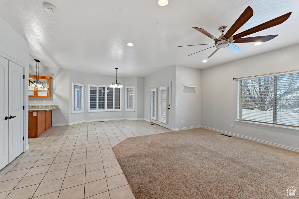 Unfurnished living room with light colored carpet and ceiling fan with notable chandelier