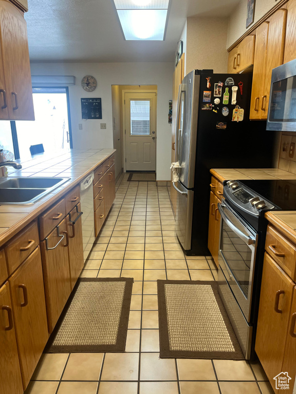 Kitchen featuring tile countertops, stainless steel appliances, sink, and light tile flooring