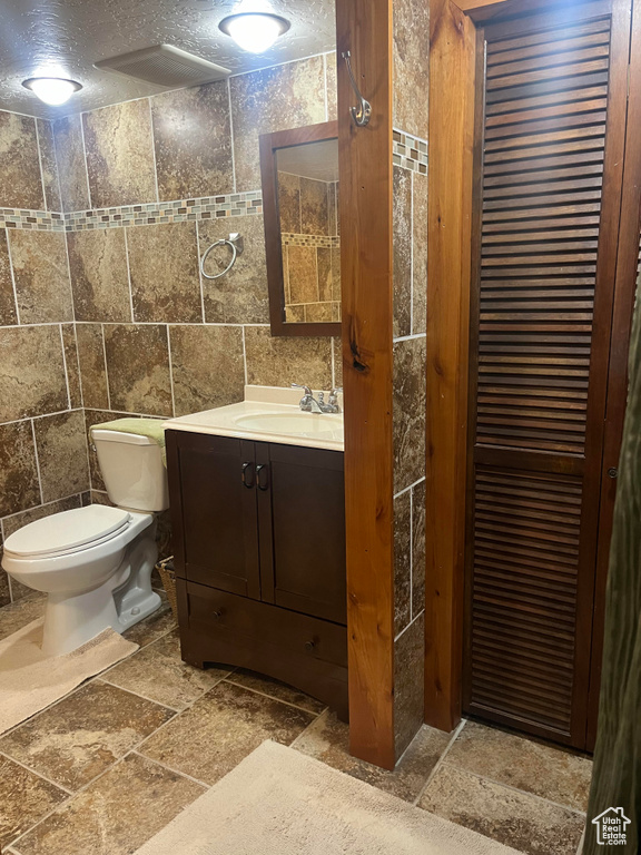 Bathroom with vanity, a textured ceiling, tile flooring, and tile walls