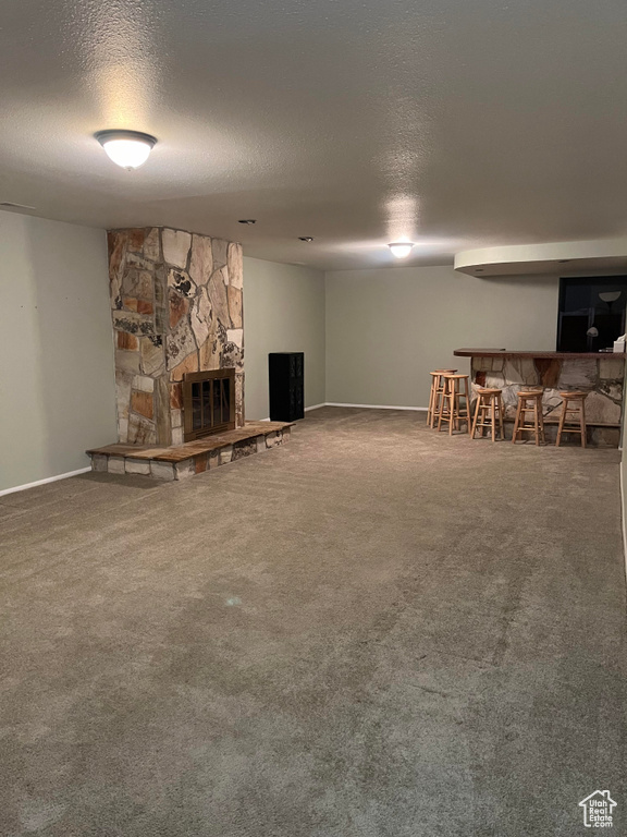 Unfurnished living room featuring a stone fireplace, dark colored carpet, a textured ceiling, and bar area
