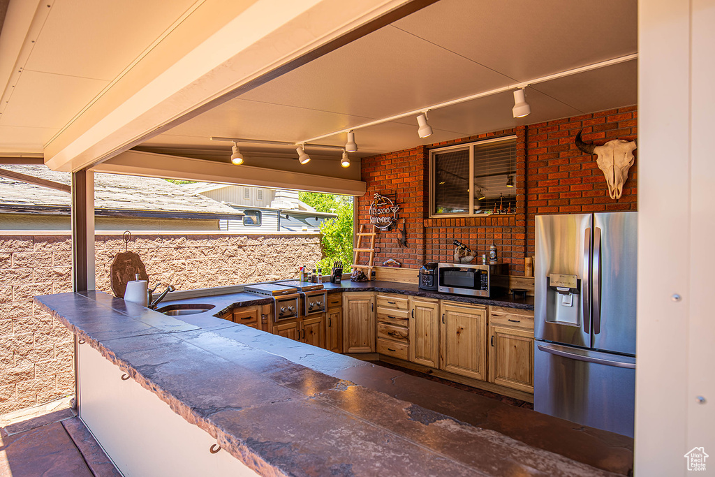 Kitchen with appliances with stainless steel finishes, sink, track lighting, and brick wall