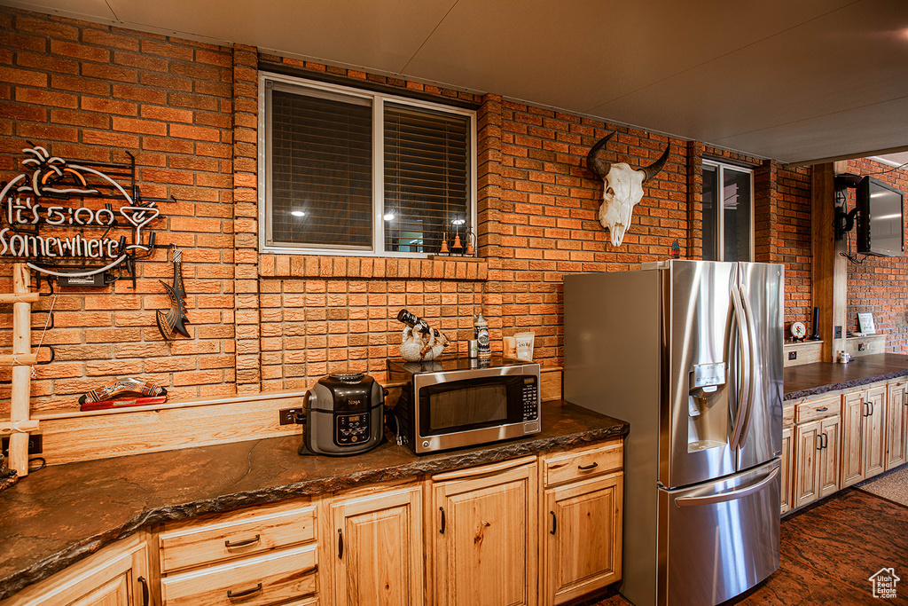 Kitchen featuring appliances with stainless steel finishes, dark stone counters, and brick wall