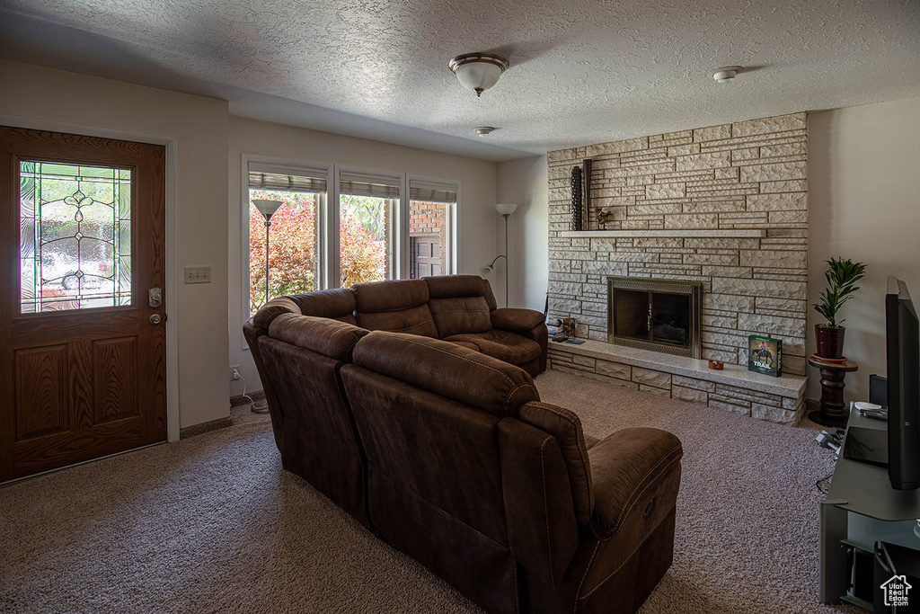 Living room with a fireplace, a textured ceiling, carpet flooring, and a wealth of natural light