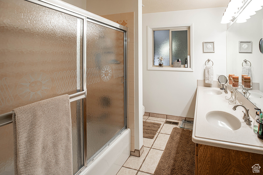 Full bathroom featuring tile flooring, large vanity, toilet, combined bath / shower with glass door, and dual sinks