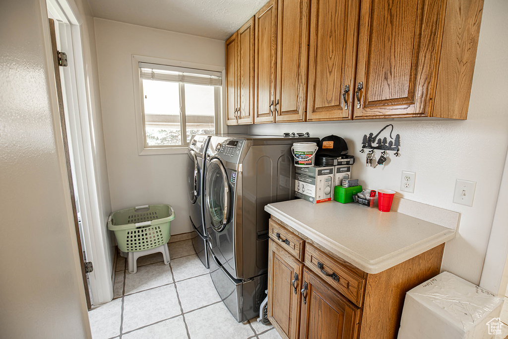 Laundry room with cabinets, washing machine and dryer, and light tile floors