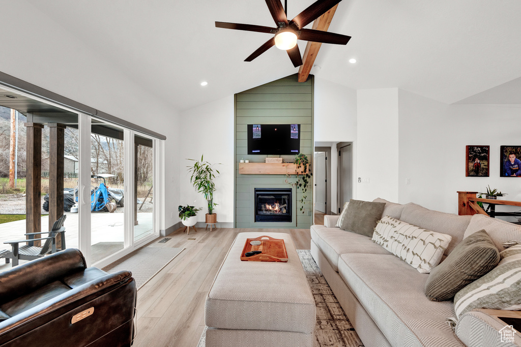 Living room featuring high vaulted ceiling, light wood-type flooring, a fireplace, beamed ceiling, and ceiling fan