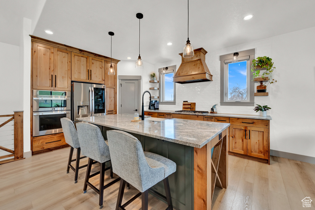 Kitchen with light stone counters, stainless steel appliances, light hardwood / wood-style flooring, and custom range hood