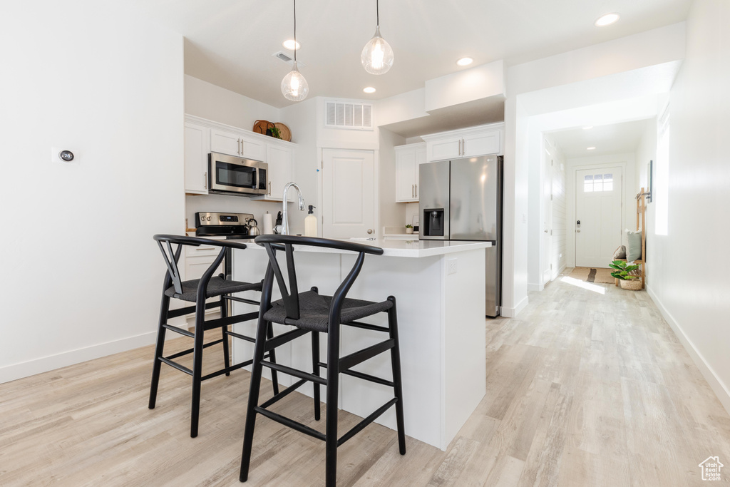 Kitchen featuring pendant lighting, appliances with stainless steel finishes, light wood-type flooring, a center island with sink, and white cabinetry