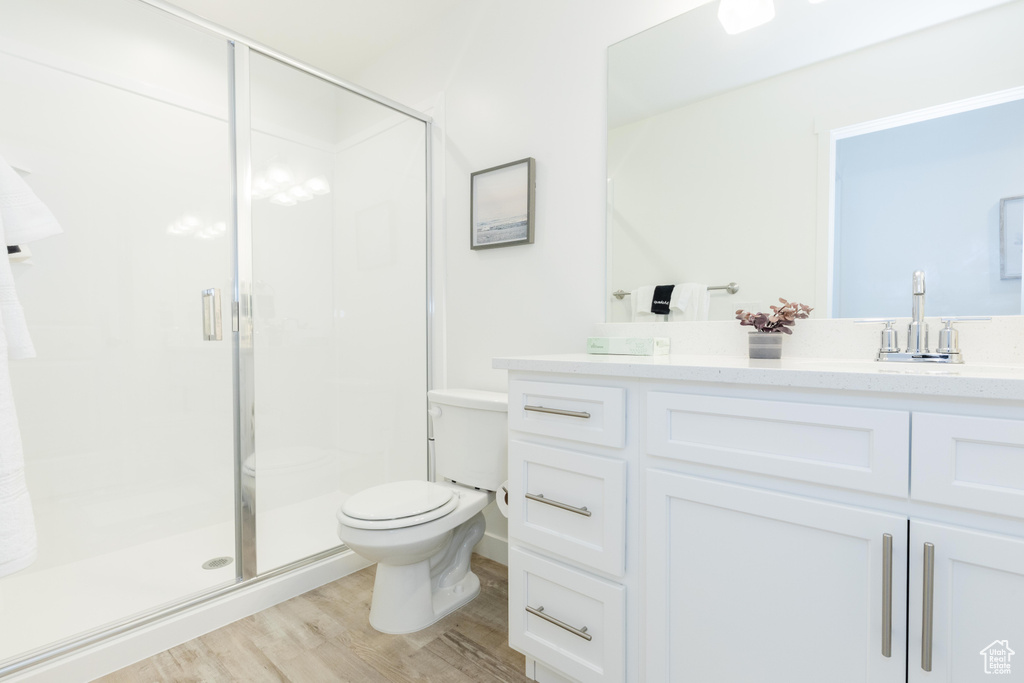 Bathroom featuring hardwood / wood-style flooring, toilet, vanity, and a shower with door