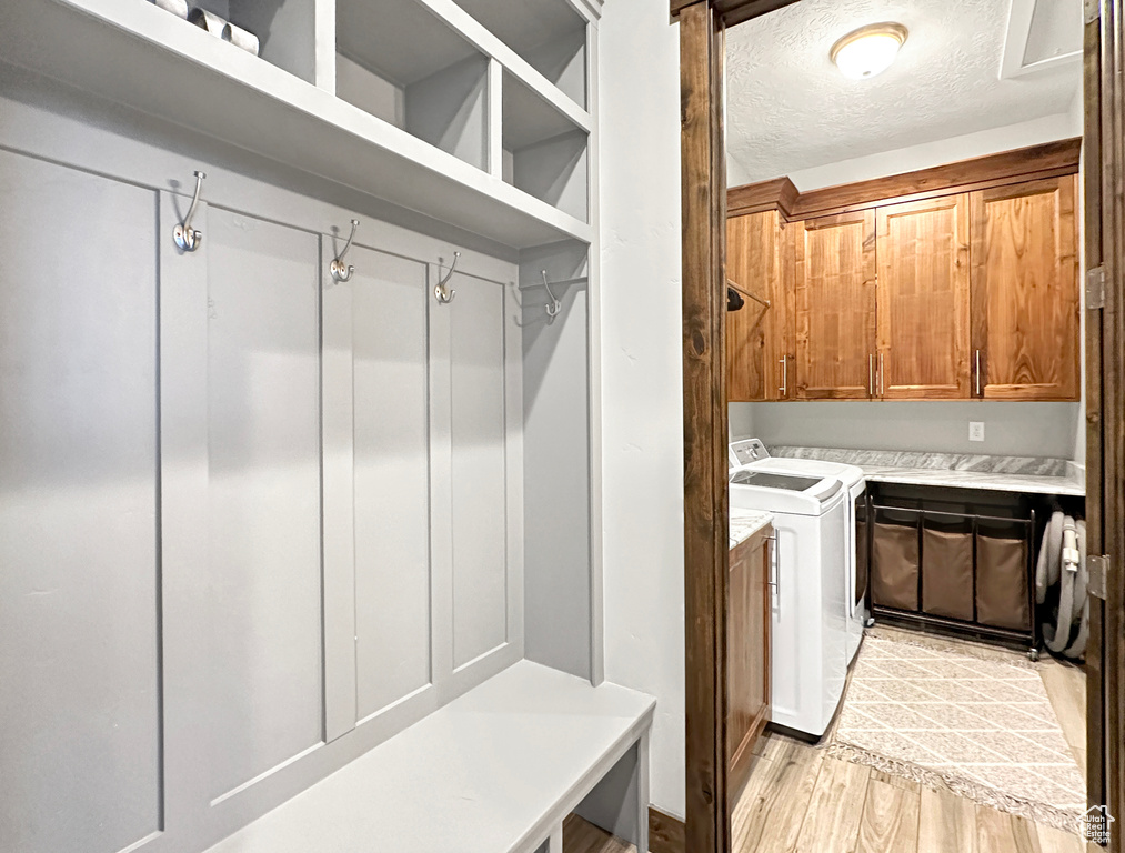 Mudroom featuring a textured ceiling, separate washer and dryer, and light hardwood / wood-style flooring