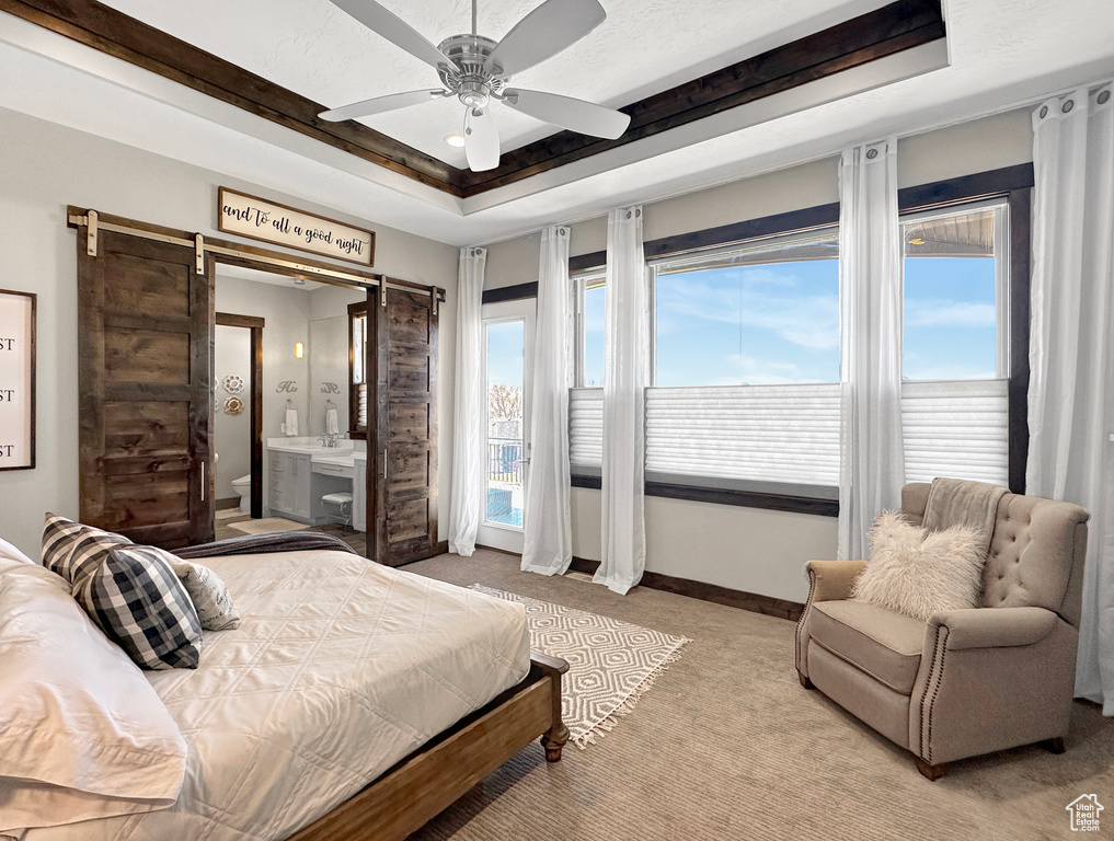 Carpeted bedroom featuring a raised ceiling, ensuite bathroom, a barn door, and ceiling fan