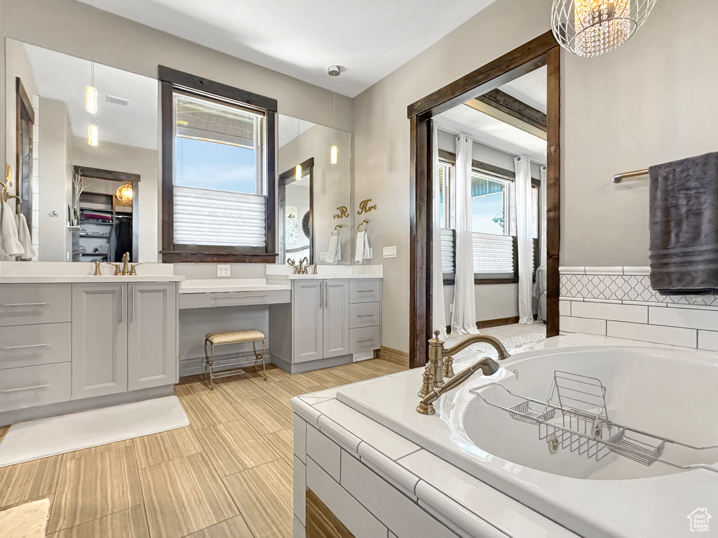 Bathroom featuring vanity, tiled tub, tile floors, and a notable chandelier