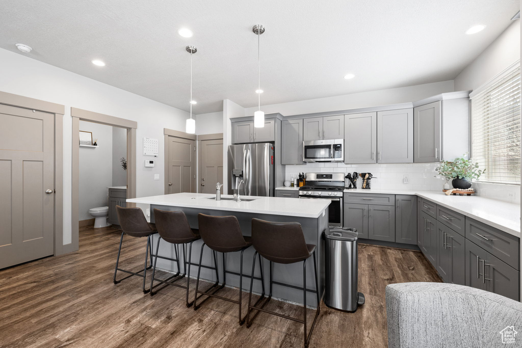 Kitchen featuring a kitchen island with sink, decorative light fixtures, stainless steel appliances, and dark hardwood / wood-style floors