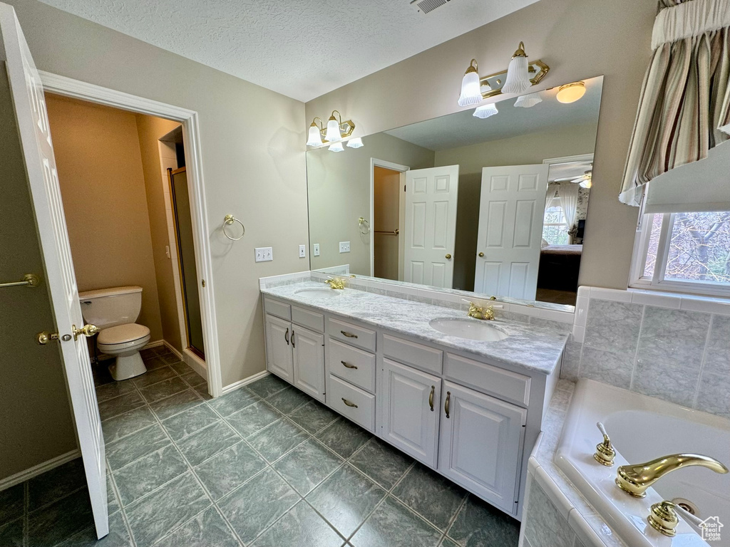 Bathroom with double sink, tile floors, a textured ceiling, vanity with extensive cabinet space, and toilet