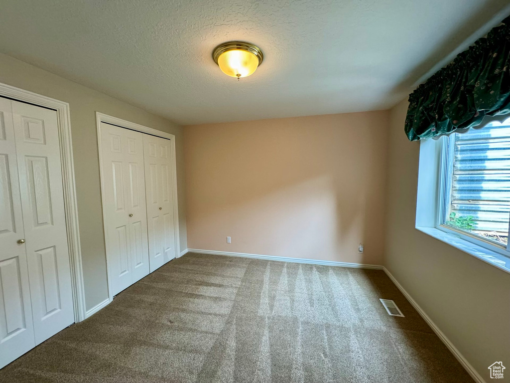 Unfurnished bedroom with two closets, a textured ceiling, and dark carpet