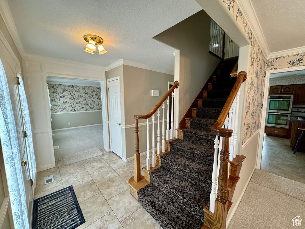 Stairs featuring light carpet, ornamental molding, and a textured ceiling