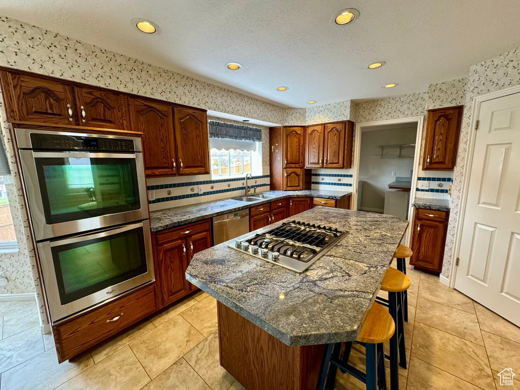 Kitchen with a kitchen island, appliances with stainless steel finishes, a breakfast bar area, backsplash, and sink