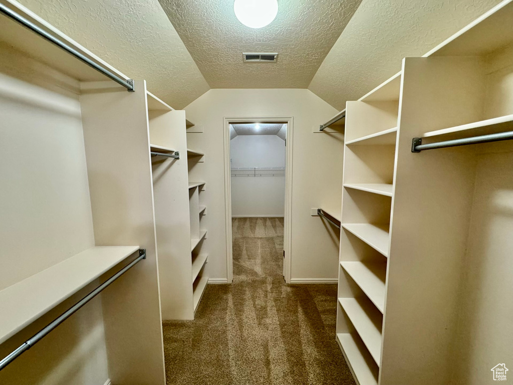 Walk in closet featuring lofted ceiling and dark colored carpet