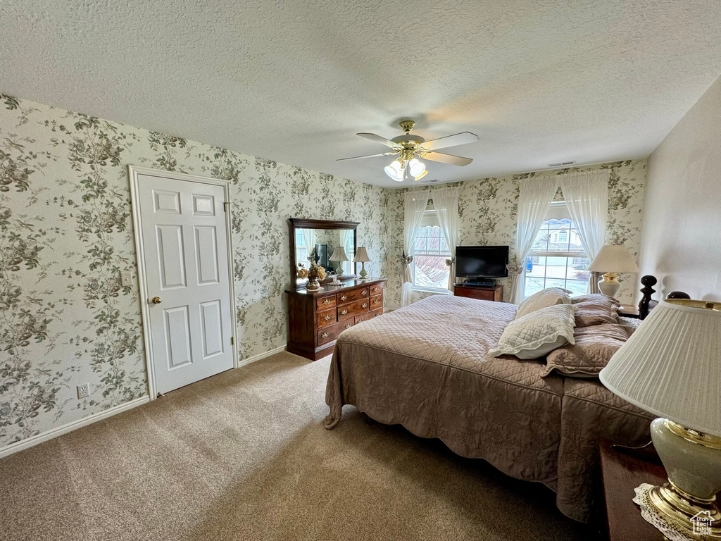 Bedroom with carpet floors, ceiling fan, and a textured ceiling