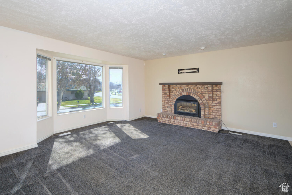 Unfurnished living room with dark colored carpet, a brick fireplace, and a textured ceiling