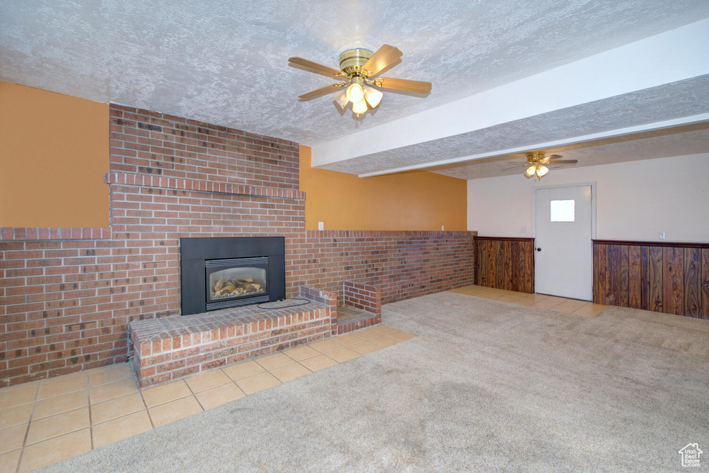Unfurnished living room featuring a textured ceiling, a brick fireplace, light carpet, and ceiling fan