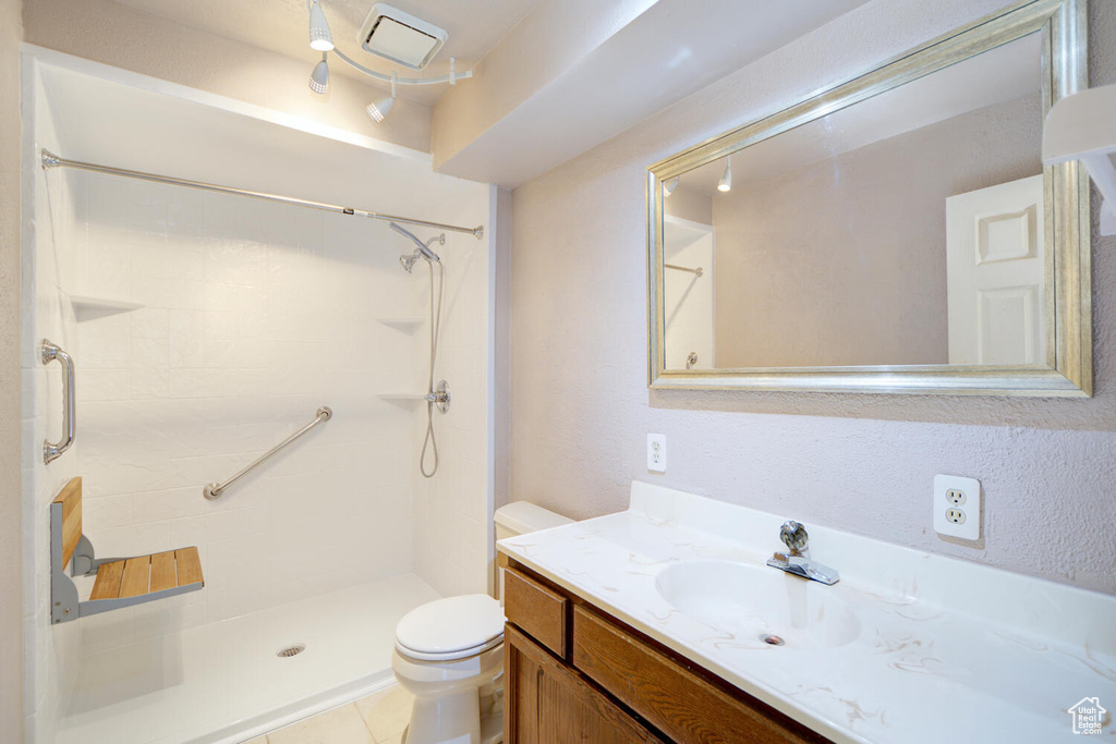 Bathroom featuring tile flooring, a tile shower, vanity, and toilet