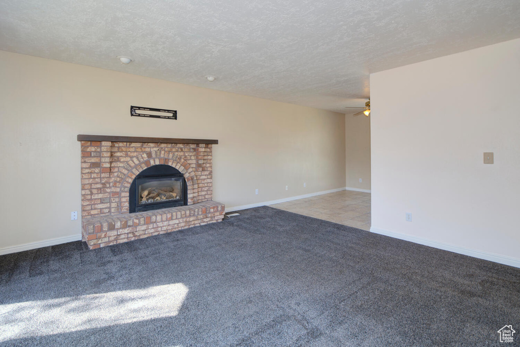 Unfurnished living room featuring a fireplace, a textured ceiling, light carpet, and ceiling fan