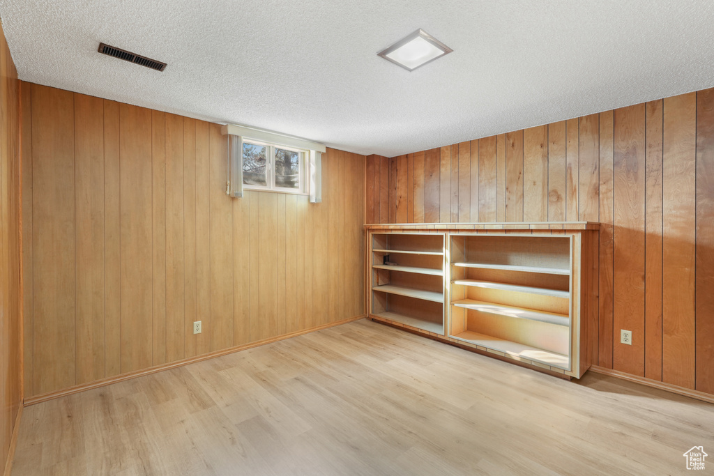 Spare room with a textured ceiling, light wood-type flooring, and wooden walls