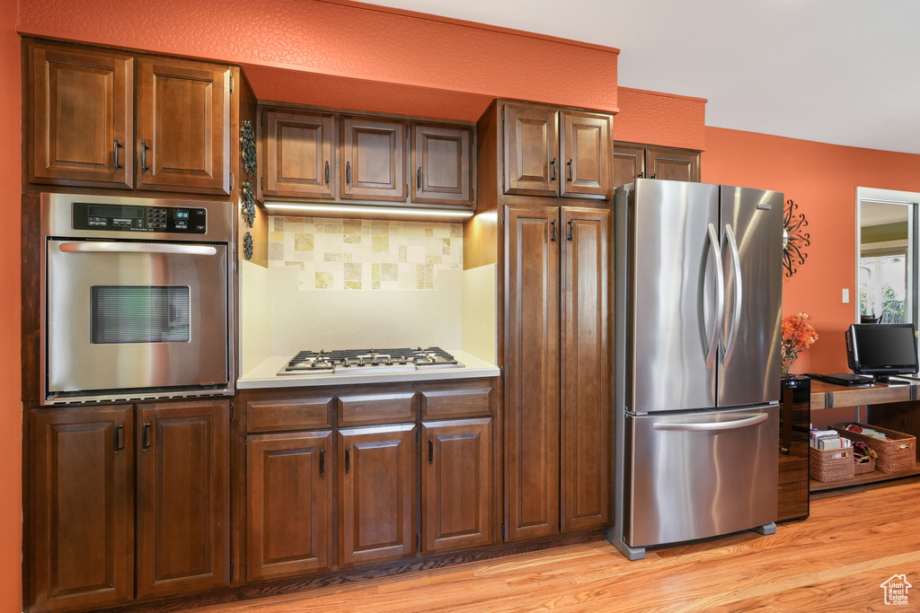 Kitchen with tasteful backsplash, light wood-type flooring, and appliances with stainless steel finishes